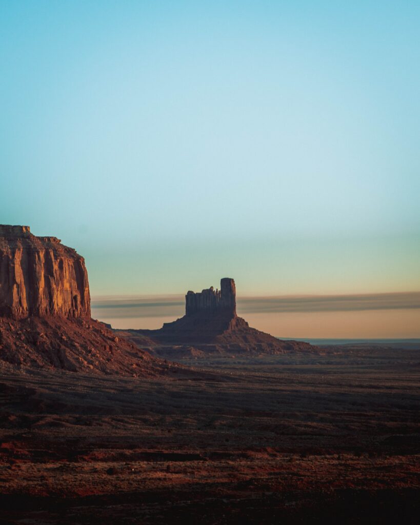 Desert valley landscape with dramatic rock formations under clear blue sky and warm sunlight Wallpaper