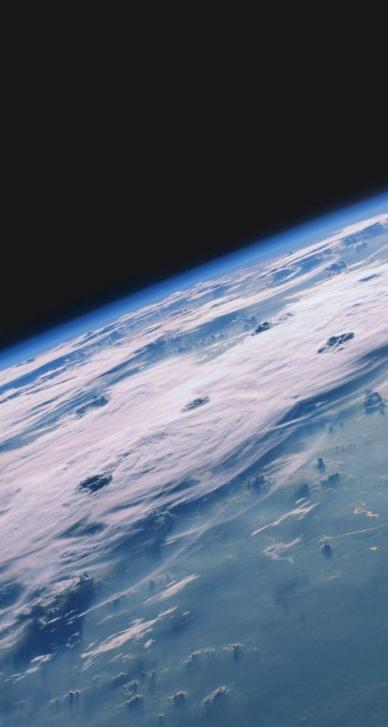 High-altitude view of Earth curvature with clouds and blue atmosphere against space background Wallpaper