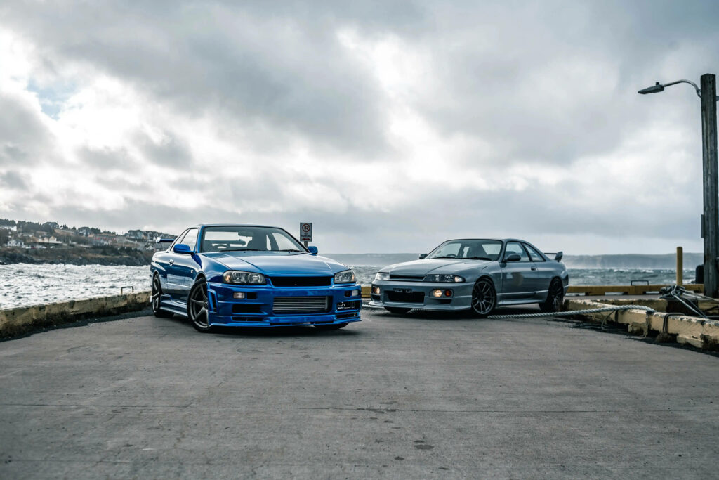 Serene GTR Car Wallpaper: Iconic Models by Waterfront Under Cloudy Sky