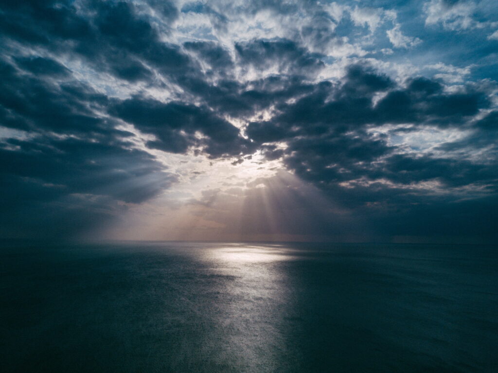 Serene Evening Beach Wallpaper: Radiant Sun Rays & Dramatic Clouds