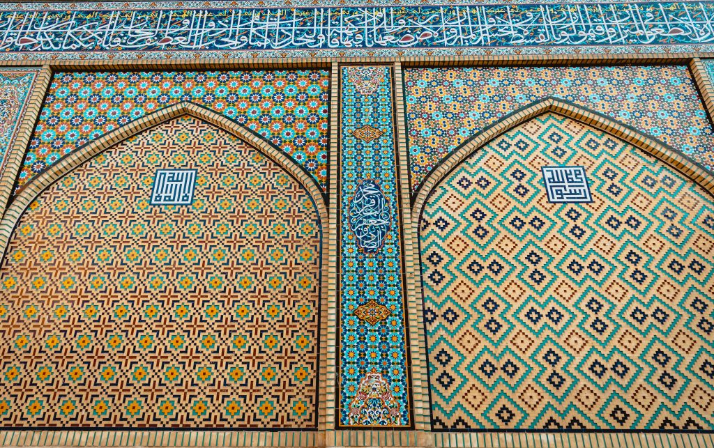 Intricate Islamic mosaic tilework with turquoise gold blue geometric patterns and Arabic calligraphy Wallpaper