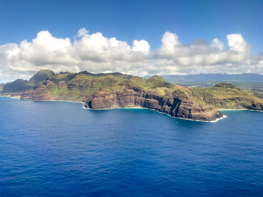 Vibrant island coastline with green cliffs and deep blue ocean under bright cloudy sky wallpaper