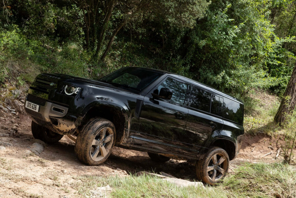 Adventurous Land Rover Defender Wallpaper: Off-Road in Lush Greenery