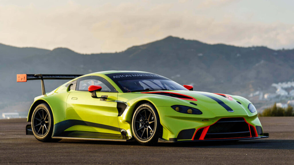 Aston Martin Vantage lime green sports car on open track with sunset and mountain background wallpaper