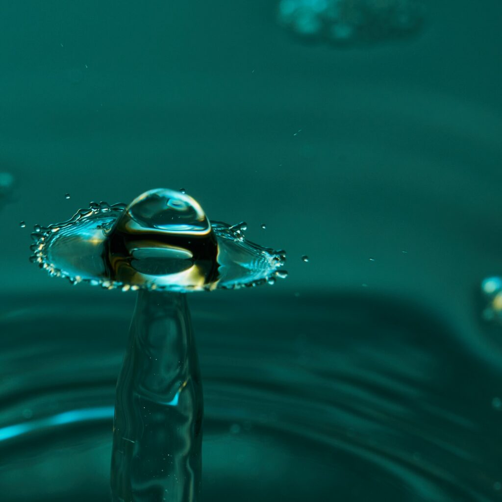 Stunning Water Droplet Collision: Macro Splash Against Teal Wallpaper
