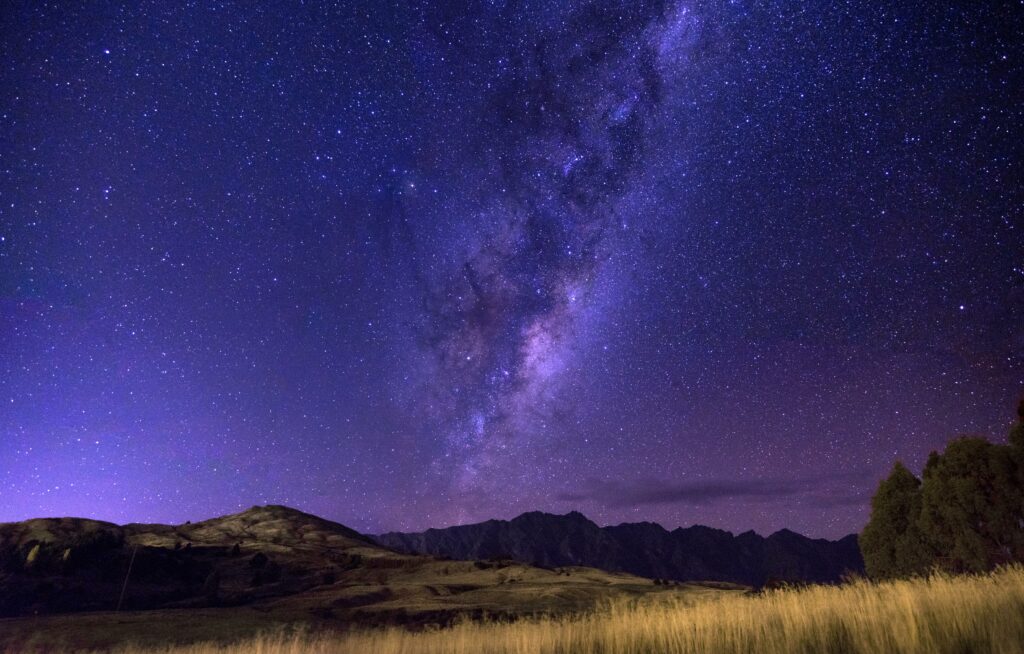 Starry sky with Milky Way over golden field and dark mountains in serene night glow wallpaper