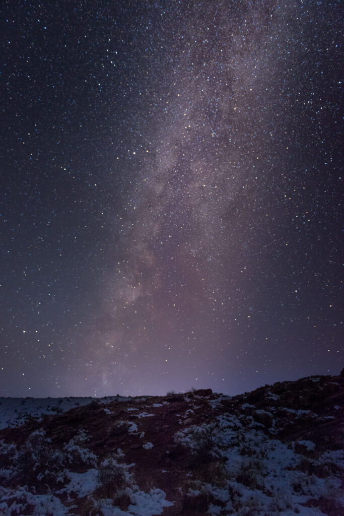 Milky Way stretches over starry night sky with rugged landscape in deep purple and blue hues wallpaper
