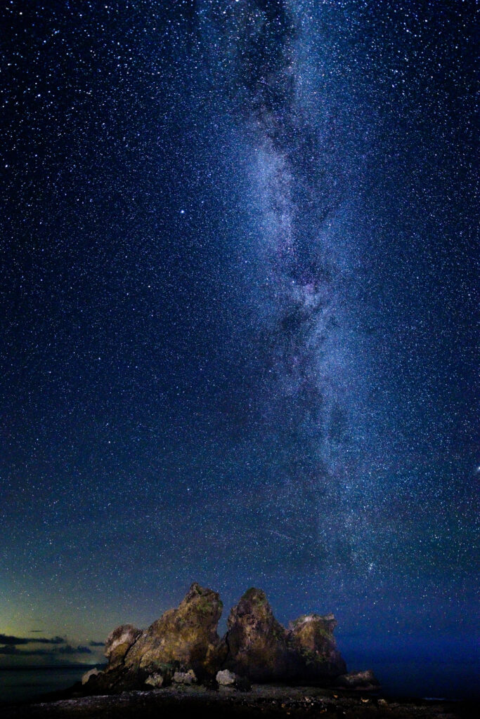 Starry night sky with Milky Way over rugged rocks serene cosmic landscape wallpaper background