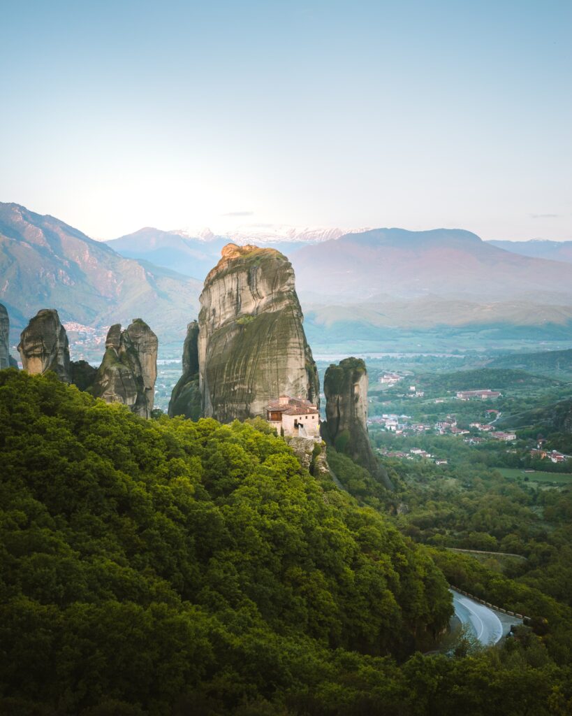 Mountain landscape with towering cliffs lush valley and quaint town under soft natural light wallpaper