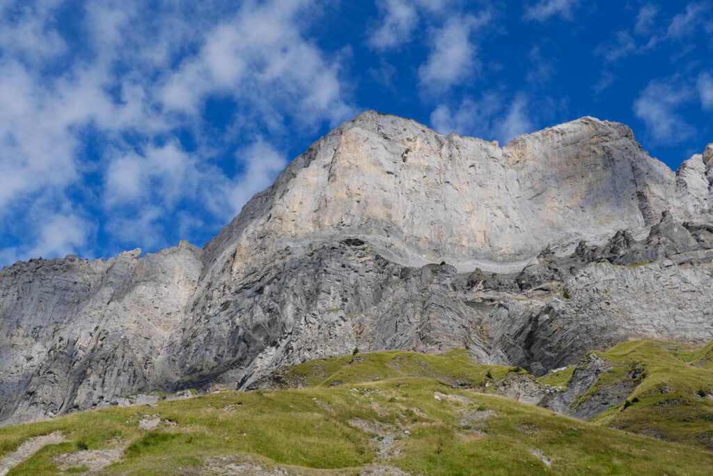 Mountain landscape with rocky cliffs and green plains under a bright blue sky with clouds Wallpaper