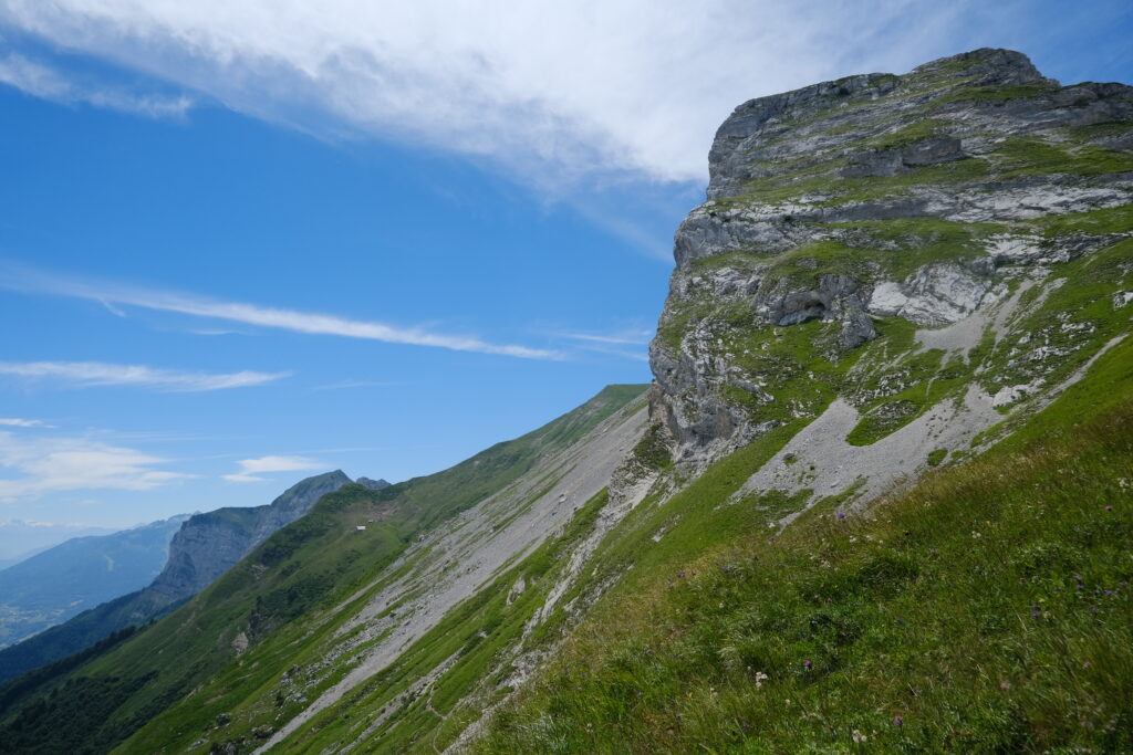 Mountain landscape with grassy slope and rugged rocks under clear blue sky wallpaper background