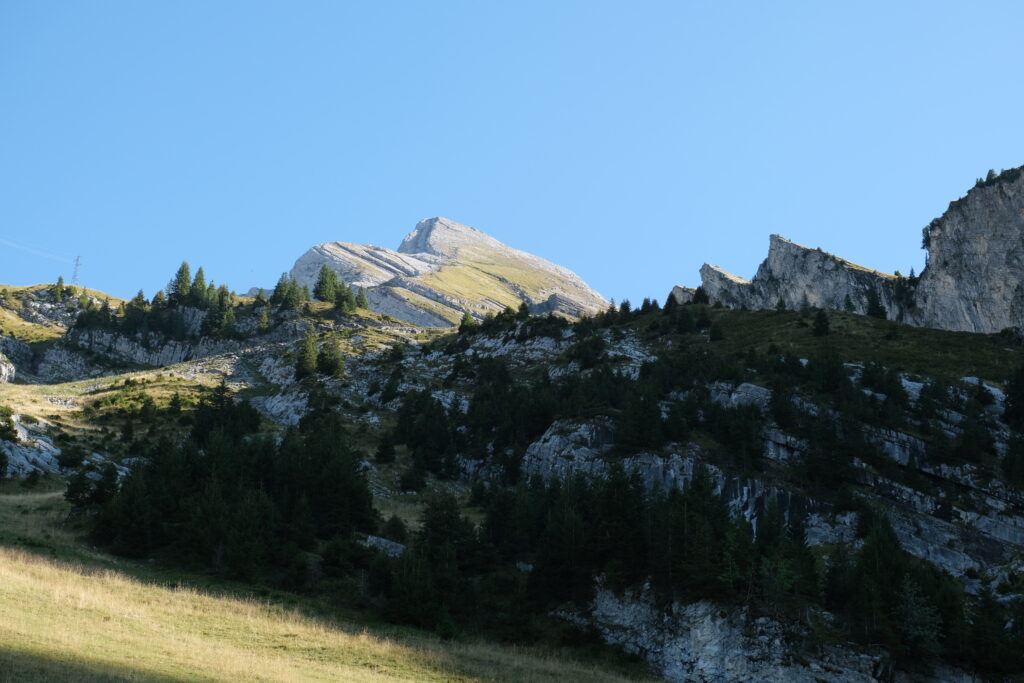 Stunning mountain landscape with rugged rocks lush green trees and dramatic shadows under blue sky Wallpaper