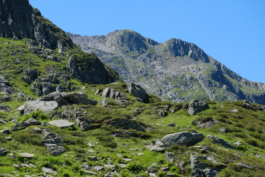 Mountain landscape wallpaper with rugged stones green grass and clear blue sky background