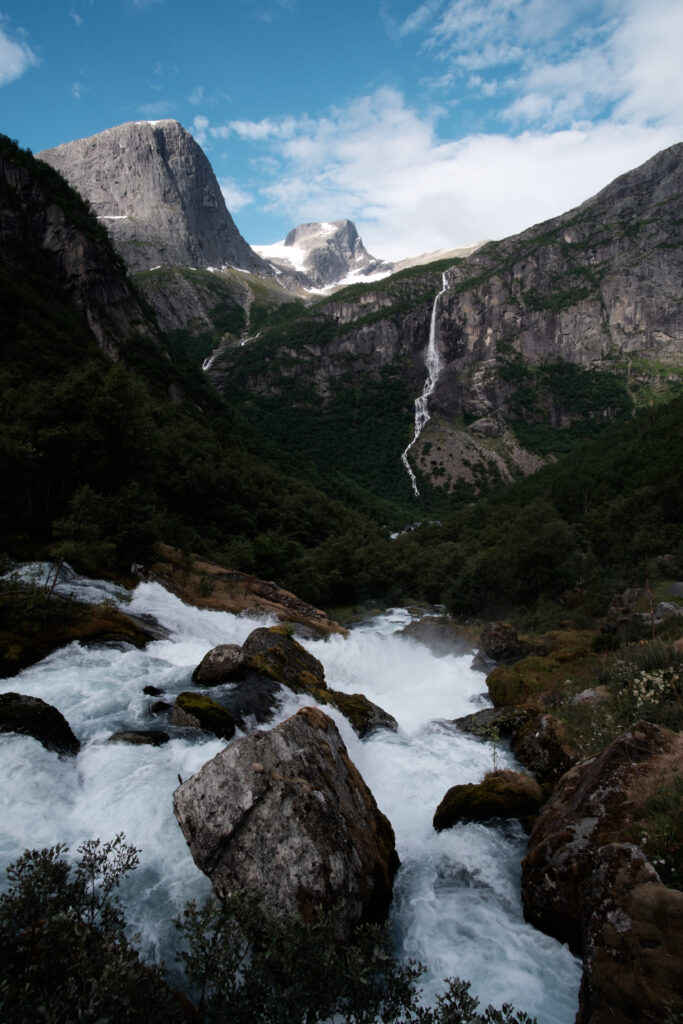 Mountain landscape wallpaper with rushing river lush greenery snow-capped peaks vibrant blue sky