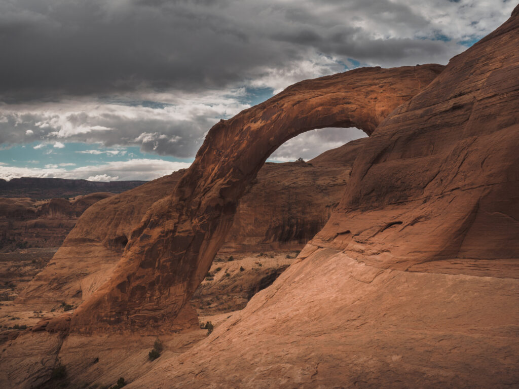 Natural arch rock formation in rugged canyon with warm tones under dramatic cloudy sky wallpaper