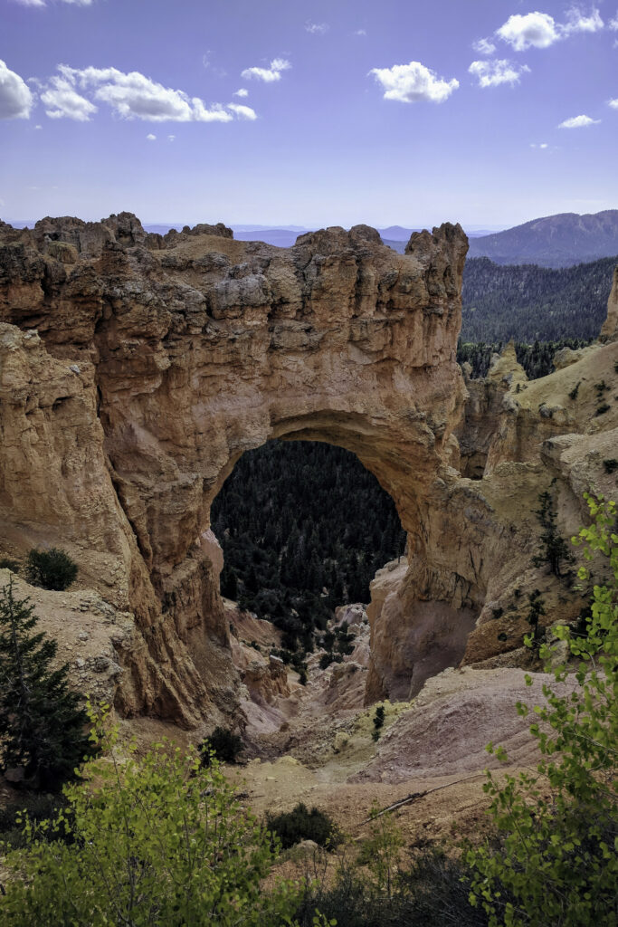 Natural rock arch with orange red hues and green trees under bright sky mountain landscape wallpaper