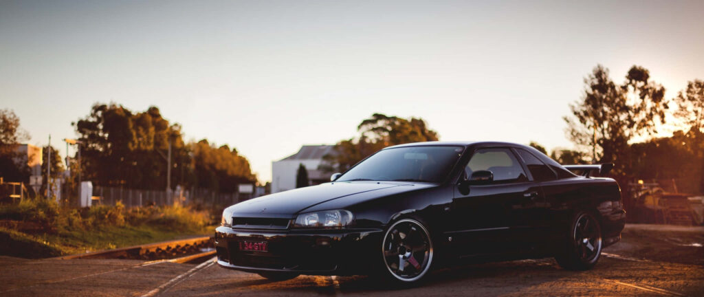 Sleek Black Nissan R33 GTR Wallpaper at Sunset on Rustic Road