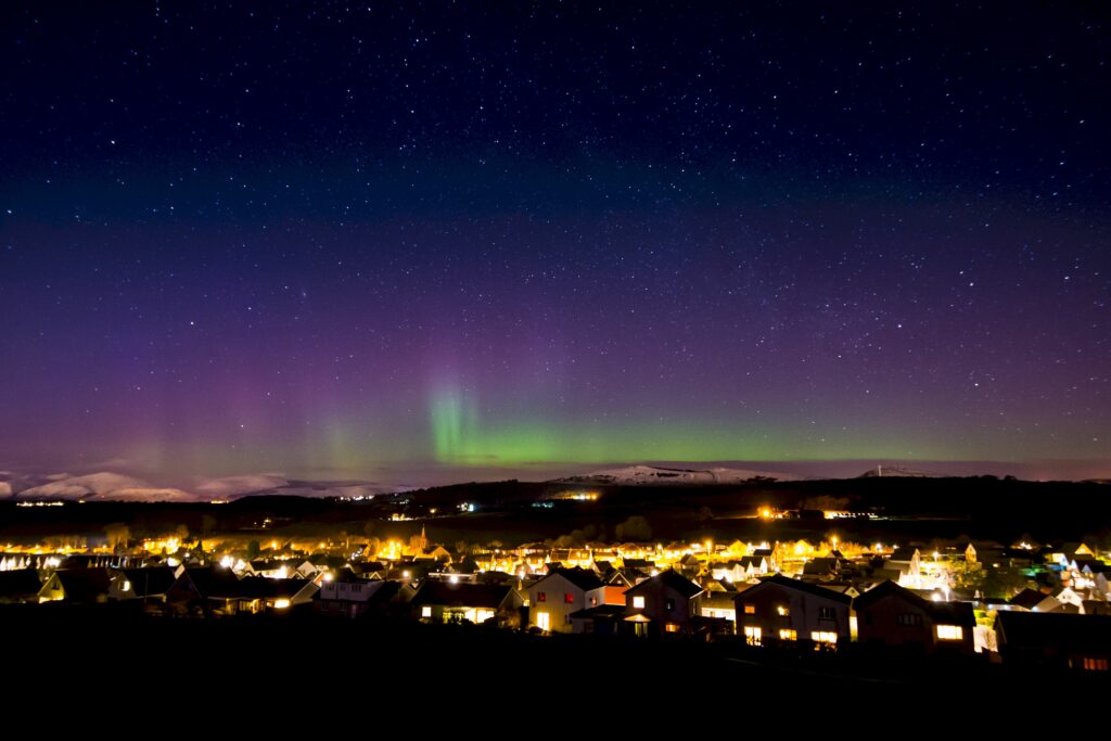 Northern lights over Scottish village vibrant green purple aurora starry sky serene night wallpaper
