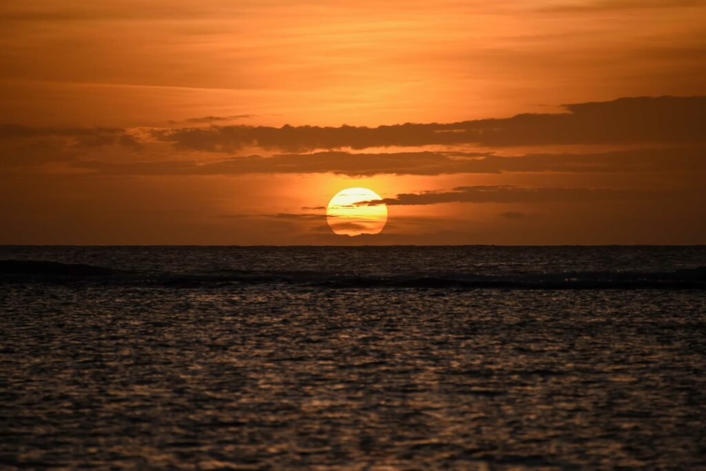 Ocean sunset wallpaper with glowing sun golden tones rippling water and silhouetted clouds