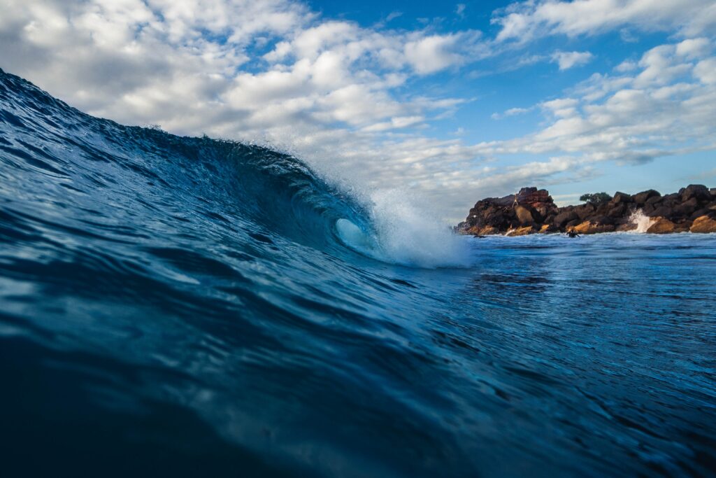 Ocean wave curling mid-surf with dynamic spray and deep blue hues under cloudy sky wallpaper