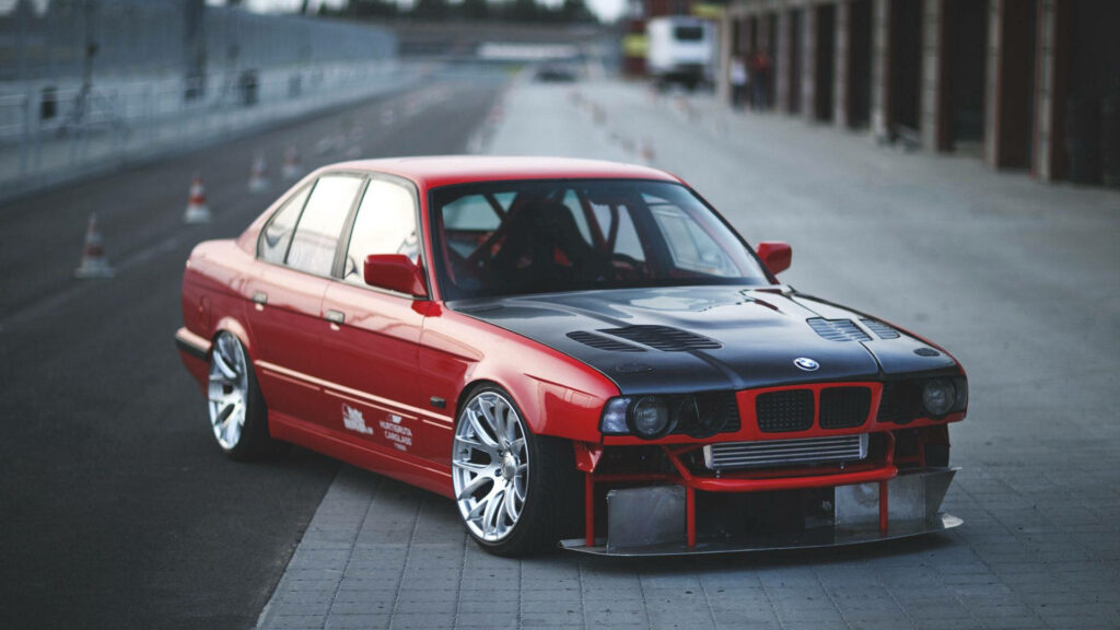 Crimson Elegance: Captivating Side Profile of a Red BMW E34, Luxuriously Parked Amidst a Scenic Stretch Wallpaper