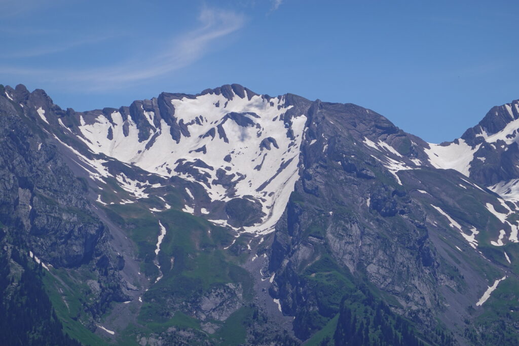 Rugged snow-capped mountain landscape with rocky textures and greenery under blue sky wallpaper