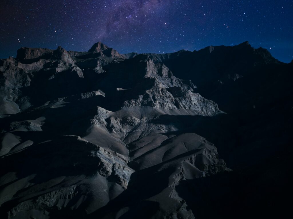 Rugged mountains under starry night sky with deep shadows and cool blue tones wallpaper background