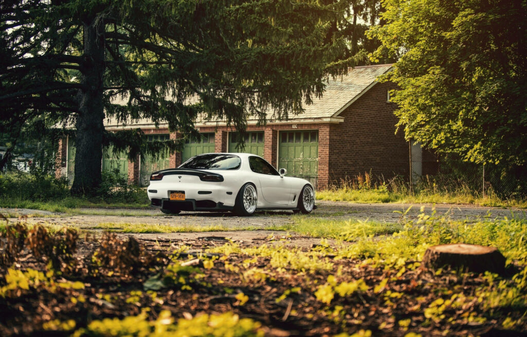 Rx7 Rising: A Stunning Snapshot of a White Mazda Rx-7 Amidst a Verdant Oasis Wallpaper