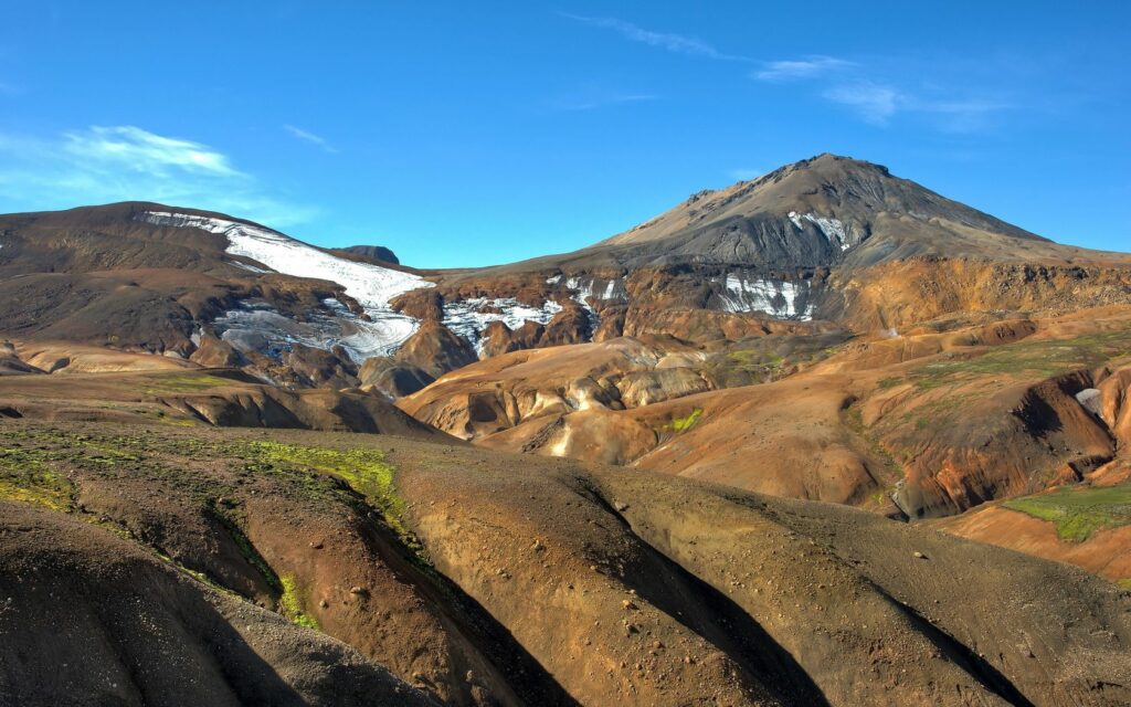 Sandy hills and rugged mountains with green vegetation and snow under clear blue sky wallpaper