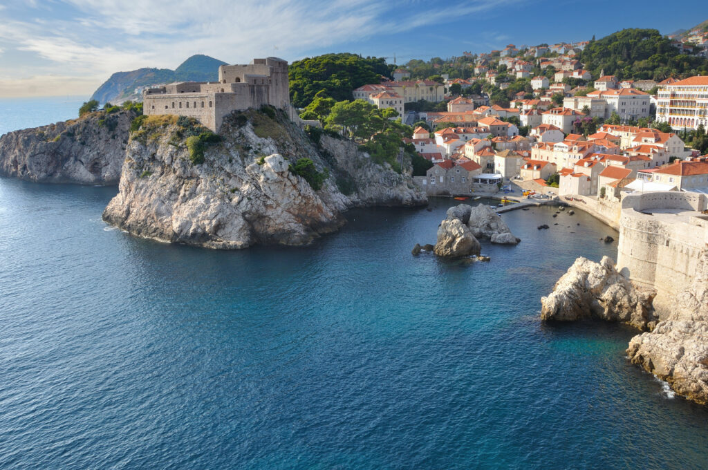 Seaside castle on rugged rocks with red rooftops and blue sea in bright sunny coastal cityscape Wallpaper