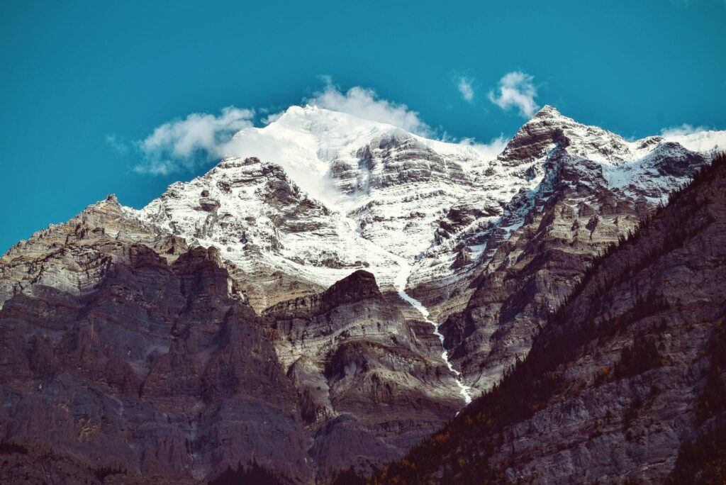 Snow-capped mountain peak with rugged slopes under clear blue sky landscape wallpaper background