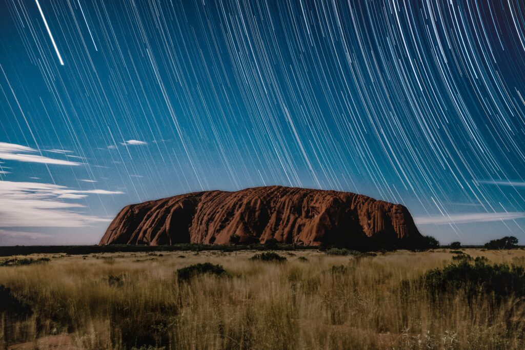 Long exposure night sky with star trails over massive rock formation scenic wallpaper background