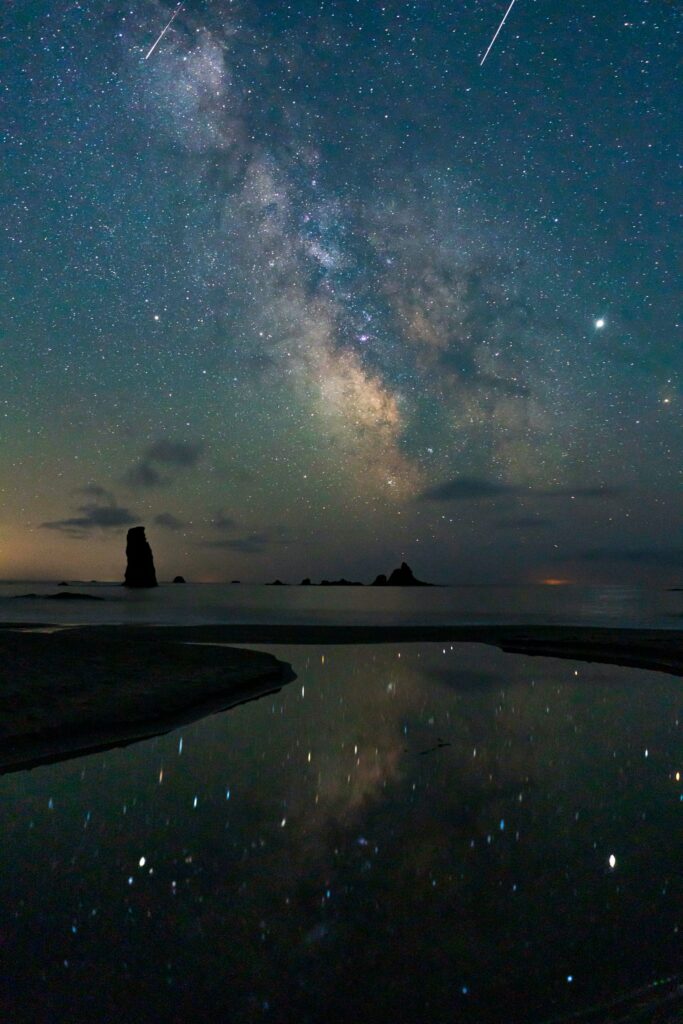 Dramatic rock formations and vibrant Milky Way stars reflected in calm water at night wallpaper