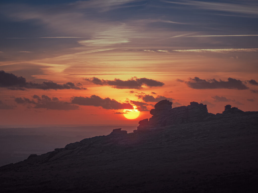 Sunset behind rugged stone formations with vibrant clouds and warm orange sky wallpaper background