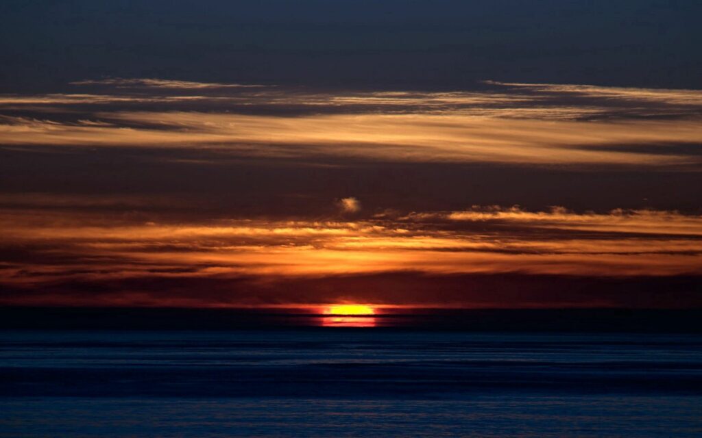 Sunset wallpaper with vibrant orange gold sky over calm blue sea creating a tranquil scene