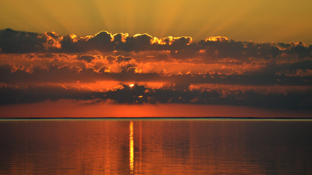 Stunning sunset over calm sea with vibrant orange gold hues and dramatic clouds wallpaper background