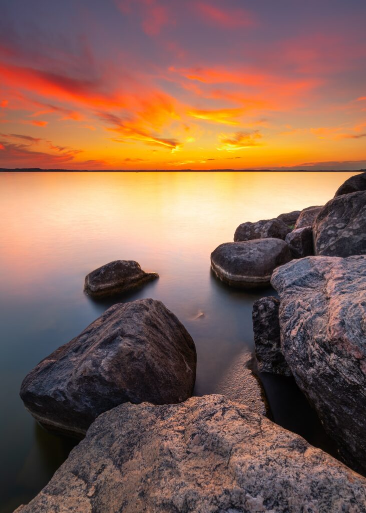 Sunset over calm sea with vibrant orange purple sky and rugged coastal rocks foreground wallpaper