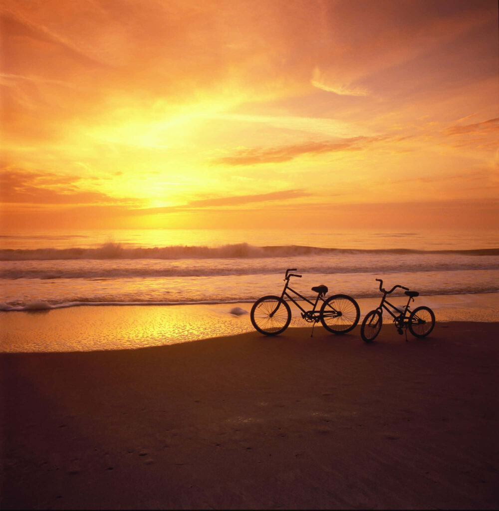 Vibrant Sunset Over Ocean with Silhouetted Bicycles on Beach Wallpaper