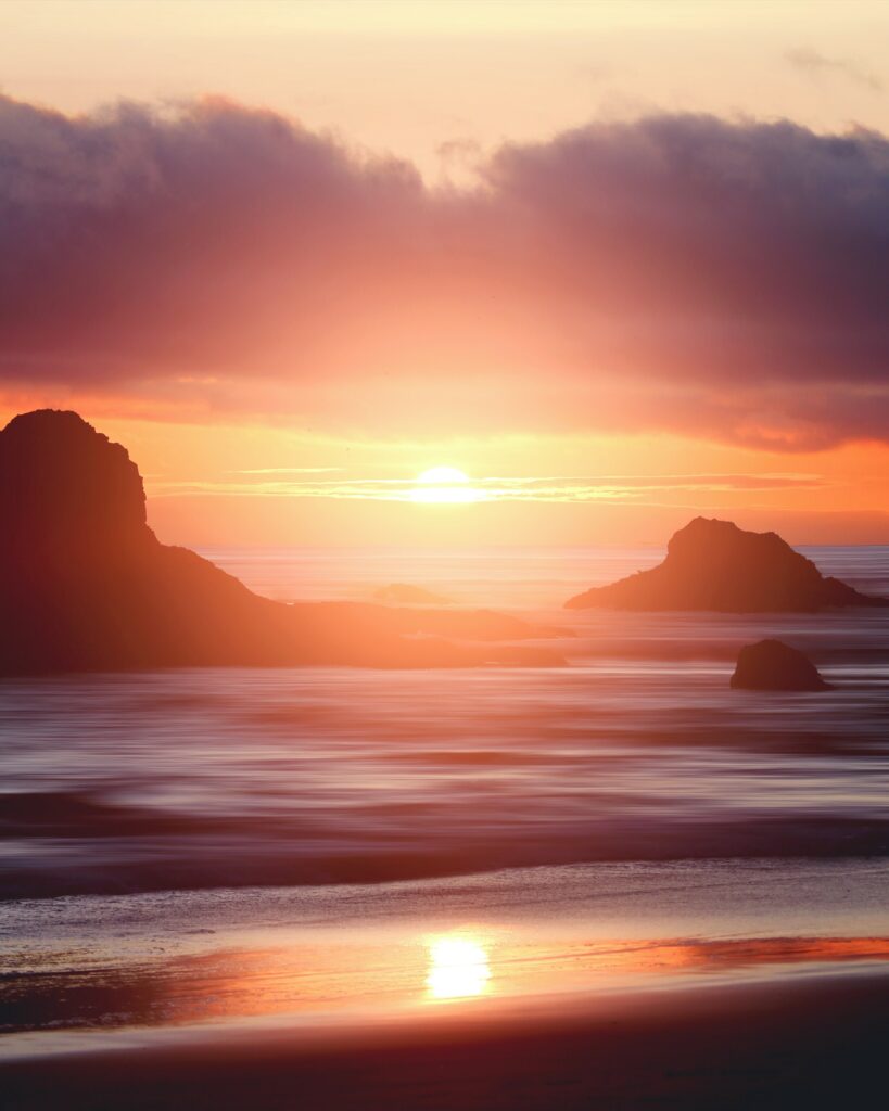 Sunset over rugged sea cliffs with orange and pink hues reflecting on calm ocean waves wallpaper