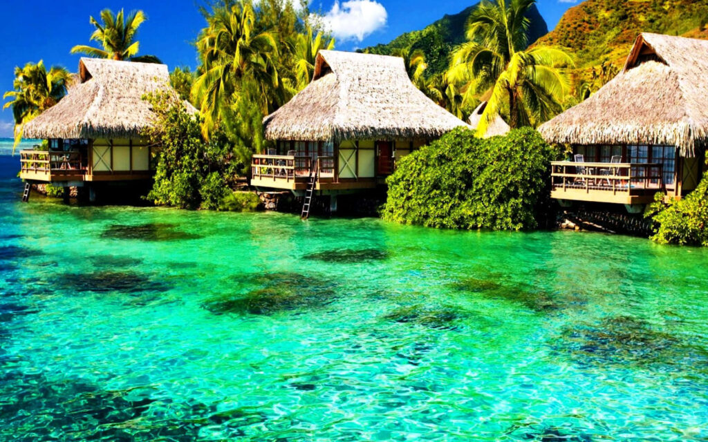 Charming Tropical Island Huts Amidst Lush Greenery and Turquoise Water Wallpaper