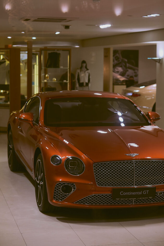 Captivating Display: A Stylish Red Orange Bentley Continental GT Shines in Showroom Ambiance Wallpaper