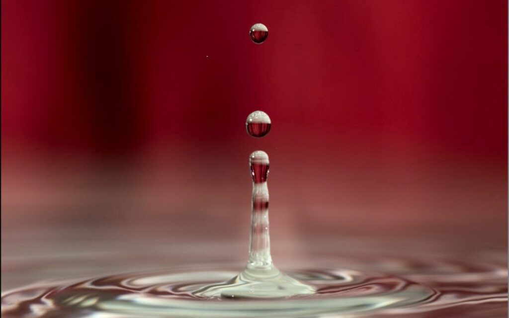 Mesmerizing Water Droplet Splash Wallpaper on Red Background