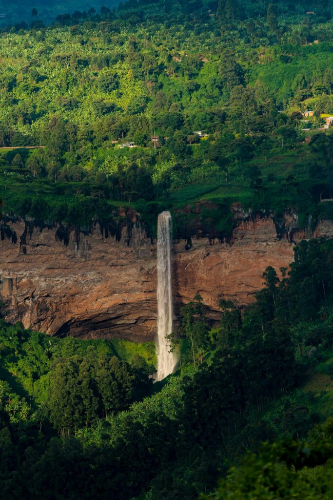Waterfall cascading down rugged cliff with lush green trees and sunlight in nature wallpaper