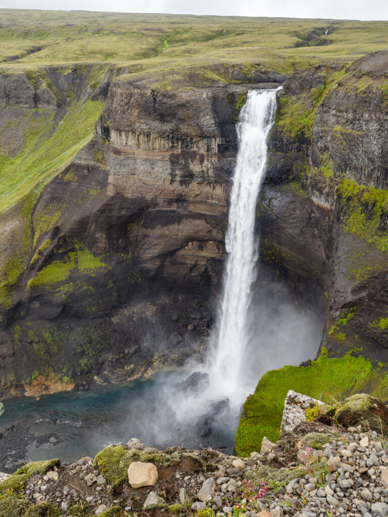 Waterfall cascading rugged cliff with vibrant green grass moss-covered rocks and rising mist Wallpaper