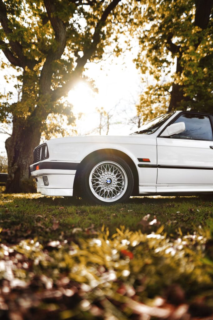 Elegant White BMW Side View with Sunlit Trees & Autumn Foliage Wallpaper