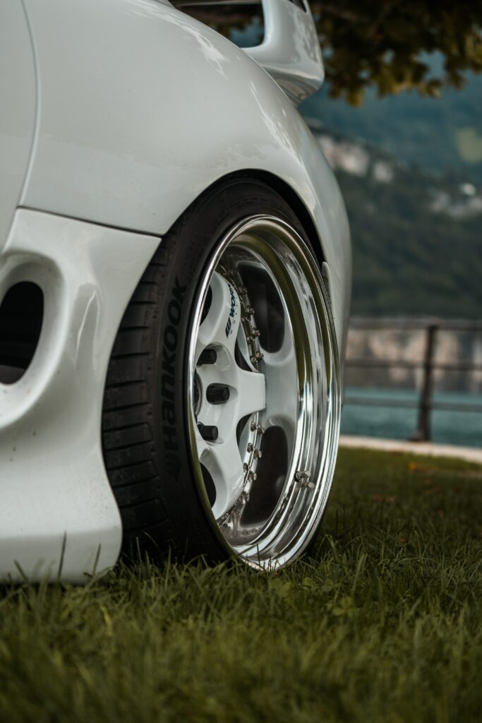 Sleek White Car Close-Up with Shiny Wheel & Serene Lakeside Background Wallpaper