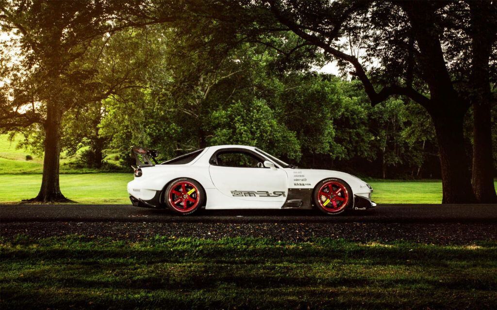 White RX7 sports car with red wheels parked on shaded forest road surrounded by green trees Wallpaper