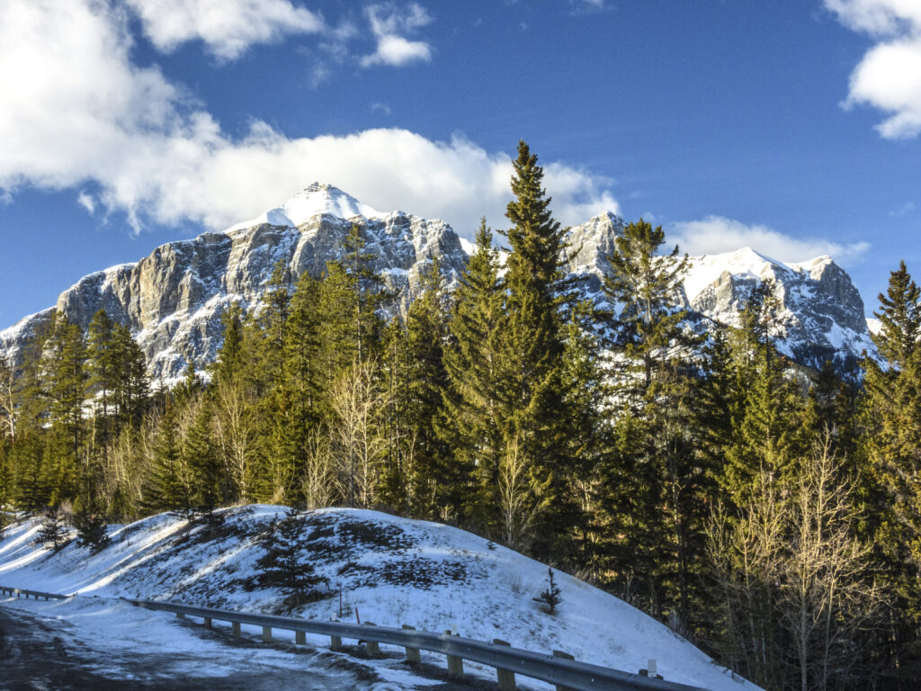 Winter landscape wallpaper with snow-capped mountains evergreen trees and winding road under blue sky