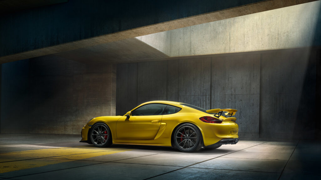 Sleek Yellow Porsche Cayman GT4 Wallpaper in Dramatic Side View
