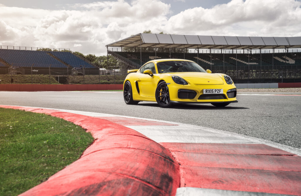 Stunning Yellow Porsche Cayman GT4 Wallpaper Against Racetrack Background